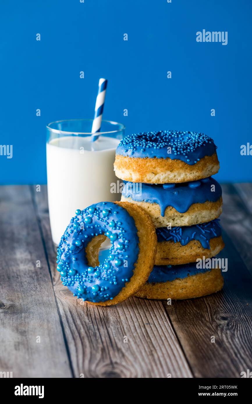 A stack of blue chocolate candy dipped donuts with a glass of milk ...