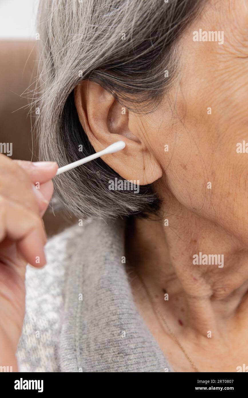 Elderly woman cleaning ear with cotton swab. Hygiene ears Stock Photo