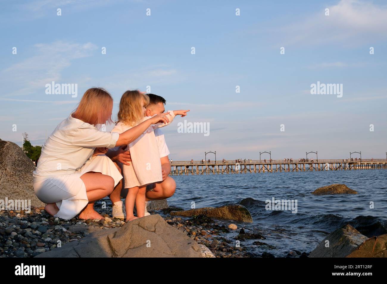 Happy family celebrating little girl's birthday on the seashore mom brings a box with cake girl opens a gift dad mom brother and sister on the ocean shore. on a sunny day Stock Photo