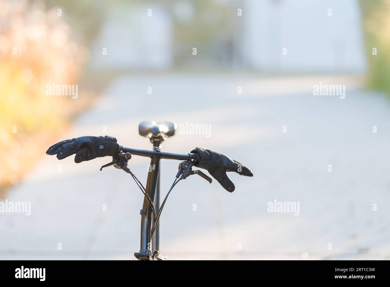 Black pair of modern synthetic gloves stuck on handlebar of folding bike standing in suburban area with blurred background on cold sunny winter Stock Photo