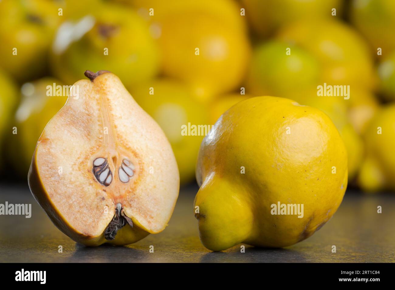 Halved and bisected quince fruit and whole fruit on dark table with pile of other quinces in blurred background Stock Photo