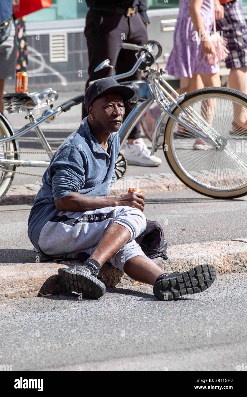 Man sitting on a curb holding a drink can at Kallio Block Party 2023 in Helsinki, Finland Stock Photo