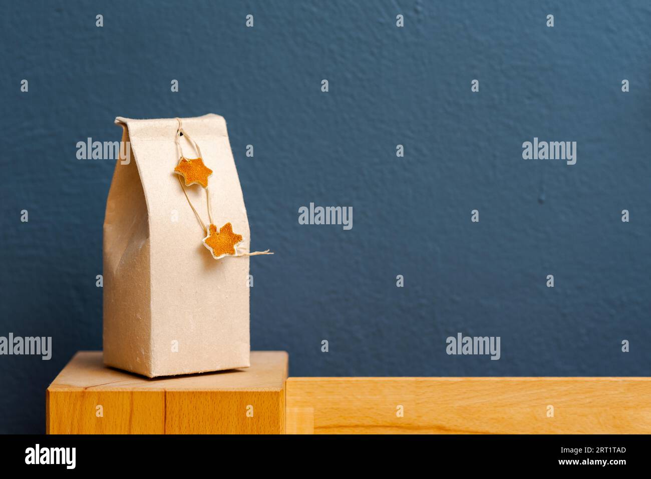 Selfmade gift box out of old beverage carton decorated with star shaped cut out dried roange peel standing on bedhead of wooden bed with copy space Stock Photo