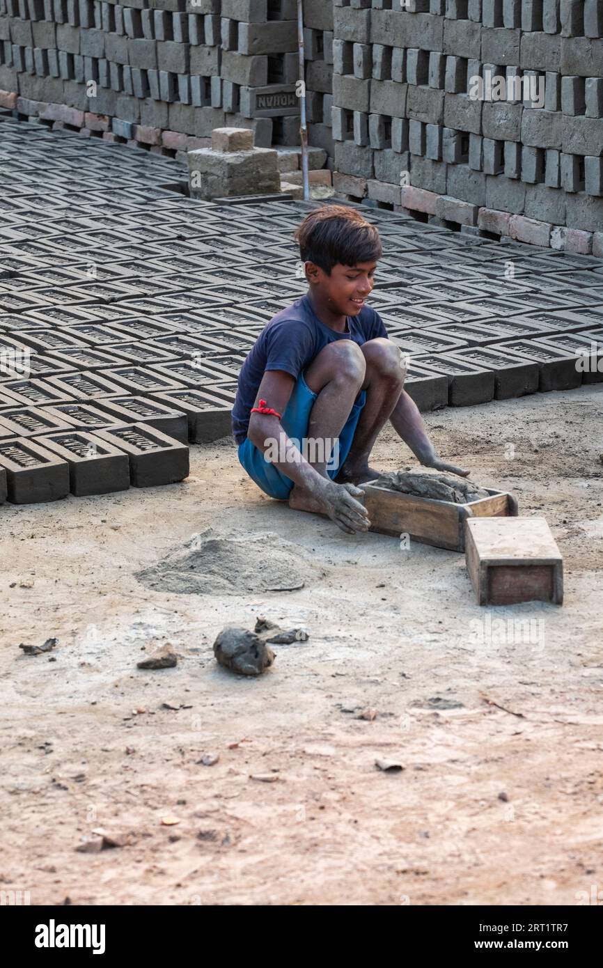 In West Bengal, India, a child laborer shapes soil in molds, part of the traditional clay brick manufacturing process, reflecting challenging realitie Stock Photo