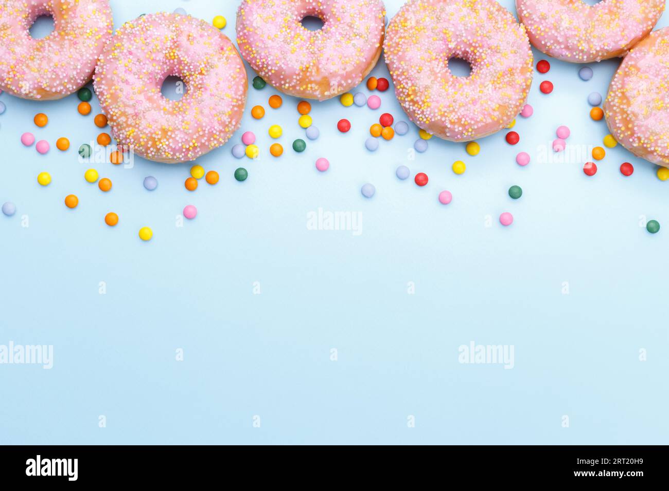 Pink doughnuts and candies on blue background, copy space flat lay Stock Photo