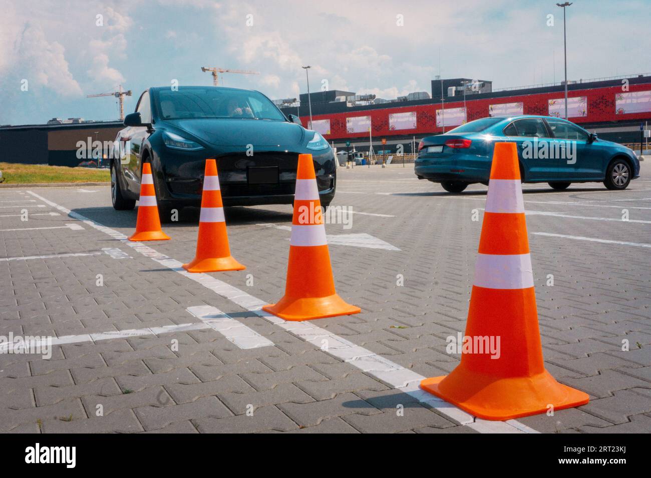 Modern car at test track, focus on traffic cones. Woman taking a