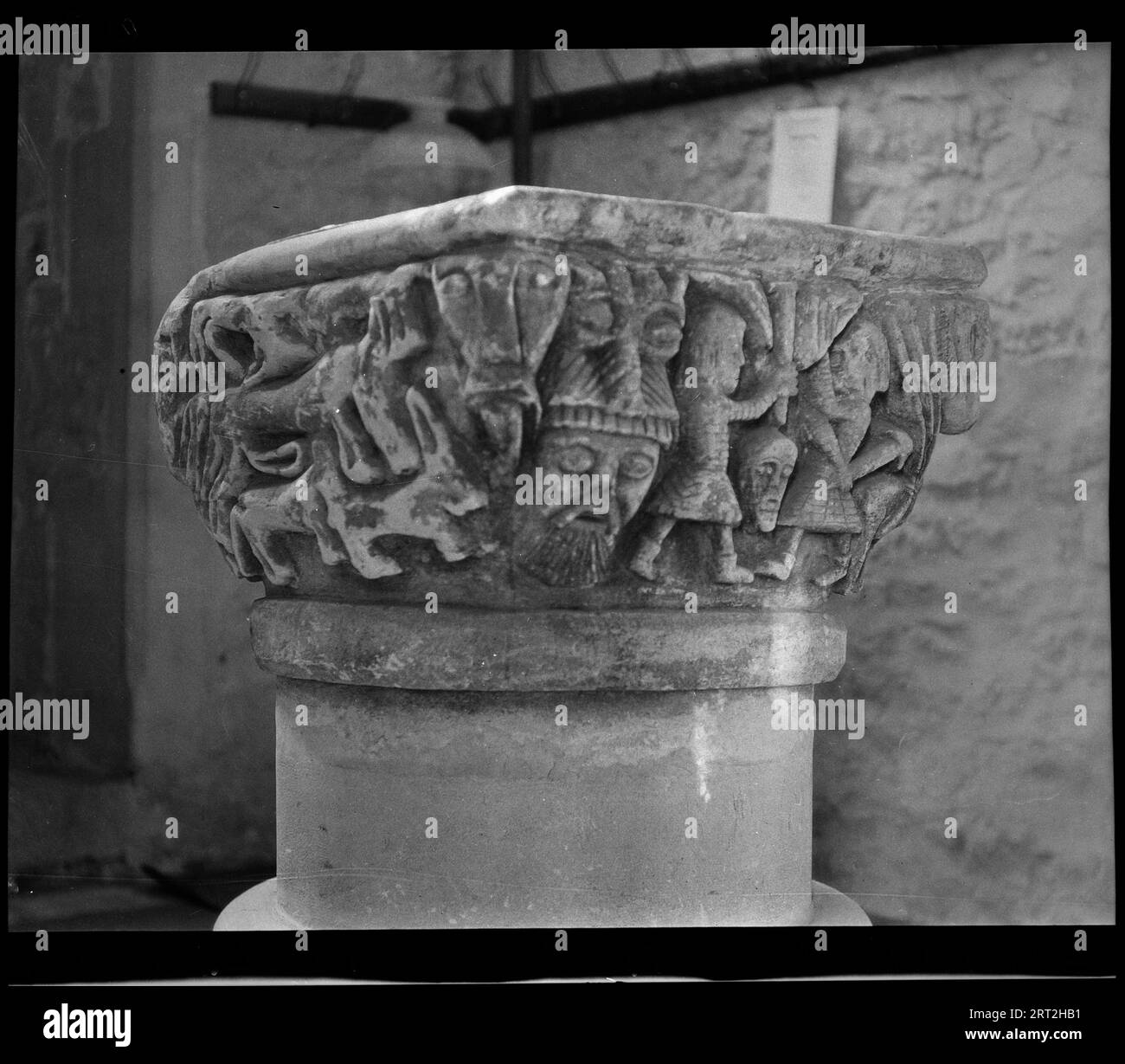 St Mary's Church, Luppitt, Luppitt, East Devon, Devon, 1940-1949. Detail of an early Norman or late Saxon font with a carved square bowl on a cylindrical shaft, the top few inches of which appear to be original and the rest modern. The angle of the image shows two sides of the bowl, one including the scene of two men fighting with shields and swords, while the other depicts wild animals. A masked face on the corner can be seen more clearly and they separate the two scenes. The church has Norman origins and was rebuilt in te 13th and 14th centuries. Stock Photo