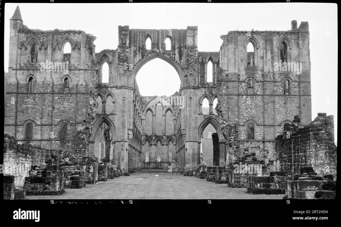 Rievaulx Abbey, Rievaulx, Ryedale, North Yorkshire, 1940-1948. View of the nave and choir taken from inside the ruins, with low rubble walls in the foreground and a clean line of sight to the end of the nave. In he centre of the image is a huge arched entrance through to the nave which is flanked on either side by columns and three storeys of arches. Further outwards from these are sections of walls with three storeys, the uppermost of which has brick of a different colour. At the very end is a small pyramidical top which is slightly higher than the rest of the wall, but this is only seen on t Stock Photo