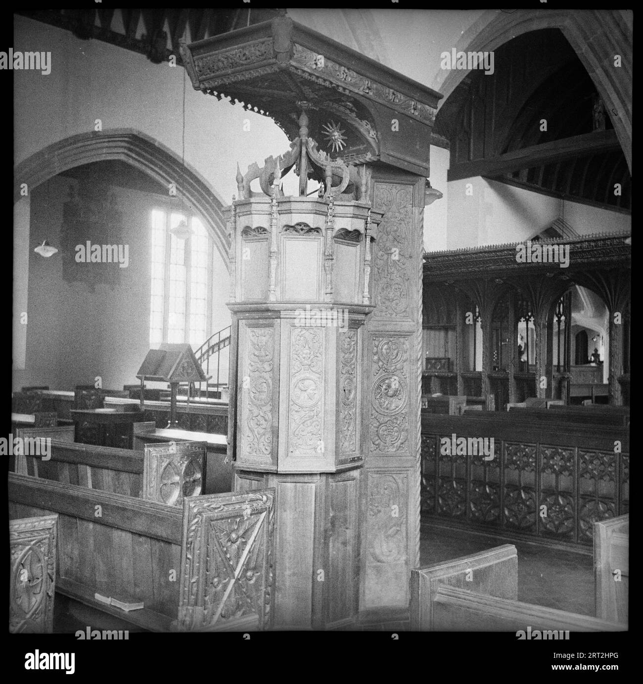 St James' Church, Swimbridge, North Devon, Devon, 1940-1962. Detail of a lead-lined Renaissance font with wooden casing that resembles a pulpit. The font has three tiers, each of which are panelled. The lower tier has plain panels, while the middle tier has decorated panels, of which some hinge open to reveal to top of the font, however in the image they are closed. The top panels are also plain, but are topped with pinnacles. Above this is an open crown over and a large rectangular canopy. In the background is a chancel screen which crosses the church and was restored in 1880. Above this is a Stock Photo