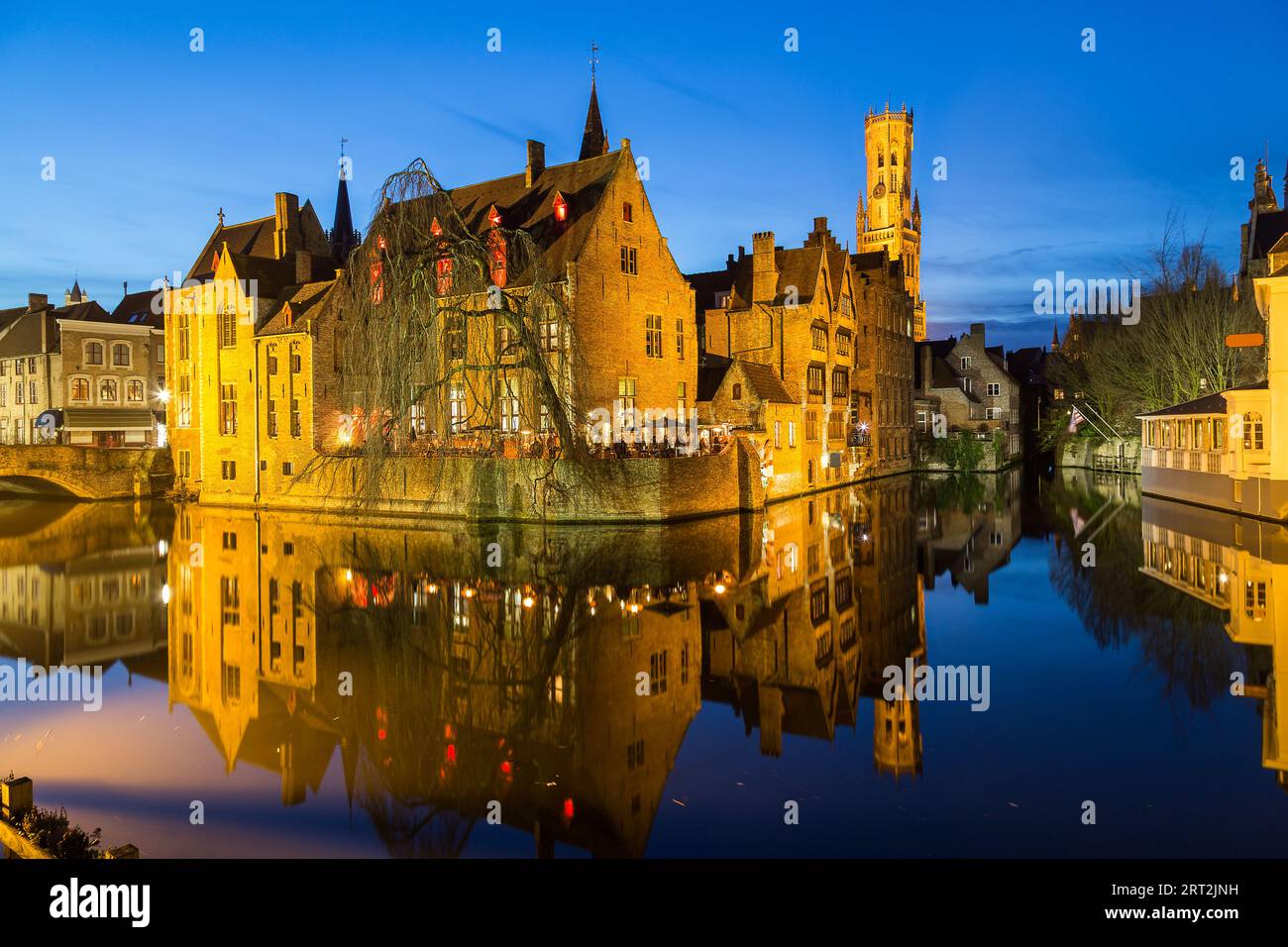 A view of Bruges from Rozenhoedkaai street at dusk. The Belfry of Bruges can be seen in the distance. Other buildings and reflections can be seen in t Stock Photo