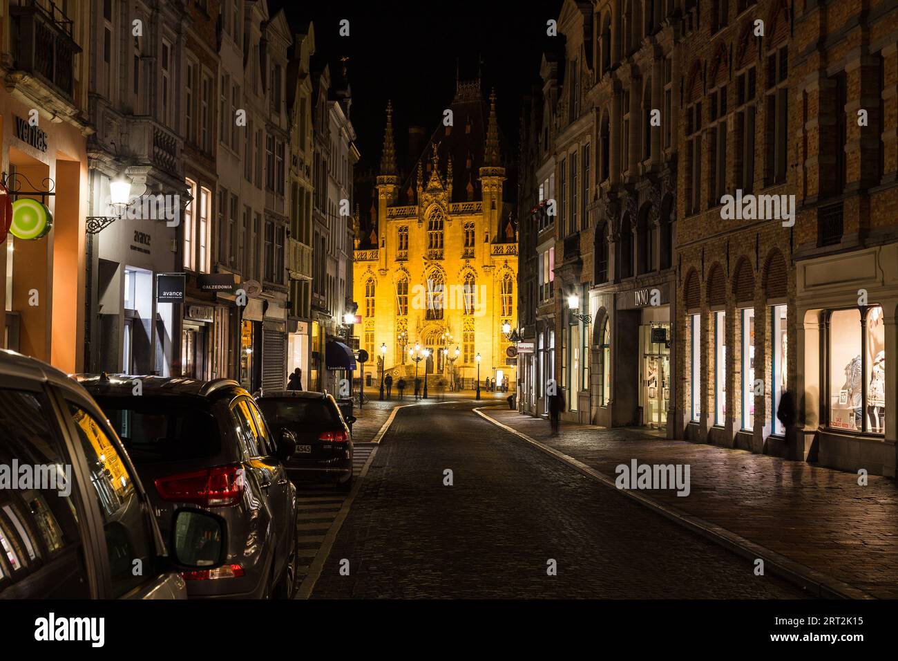 BRUGES, BELGIUM - 19th FEBRUARY 2016: A view along Steenstraat  at night towards St. Salvator's Cathedral. Shops, cars and the blur of people can be s Stock Photo