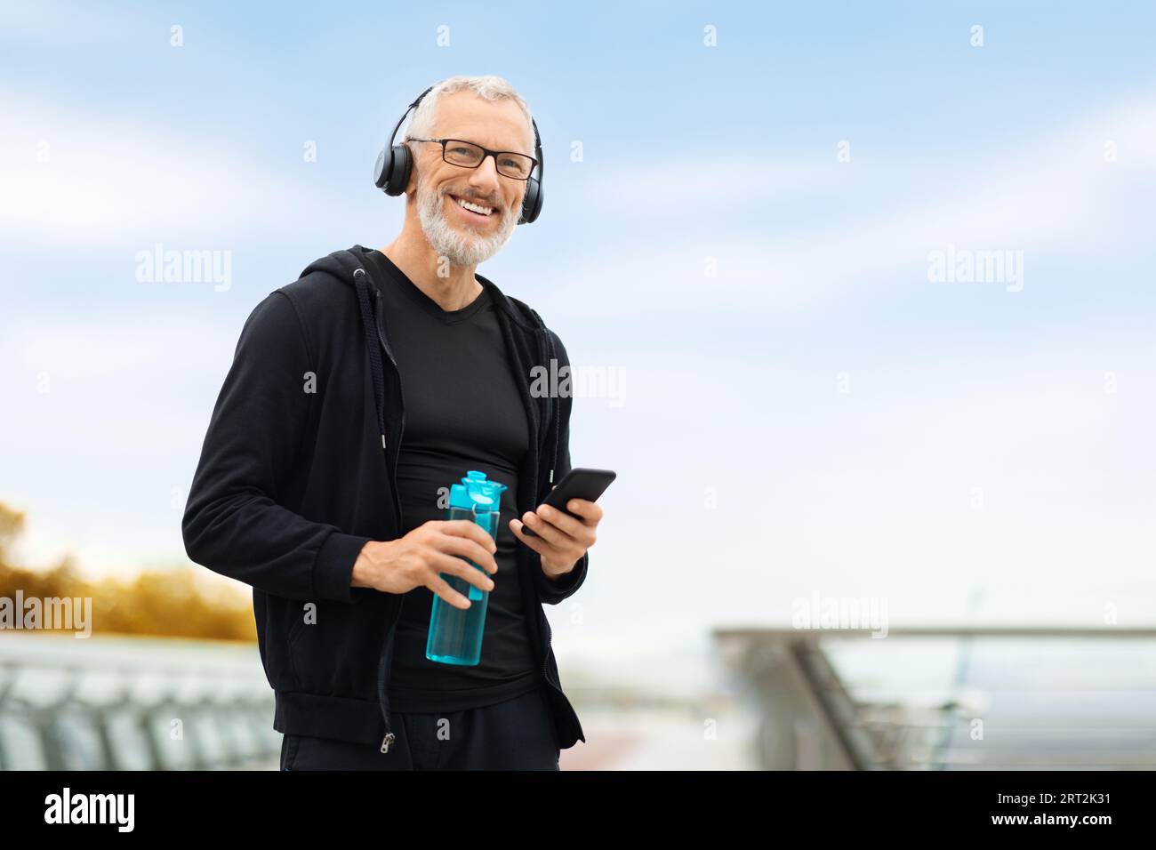 Senior man using phone while have outdoor workout, drinking water Stock Photo