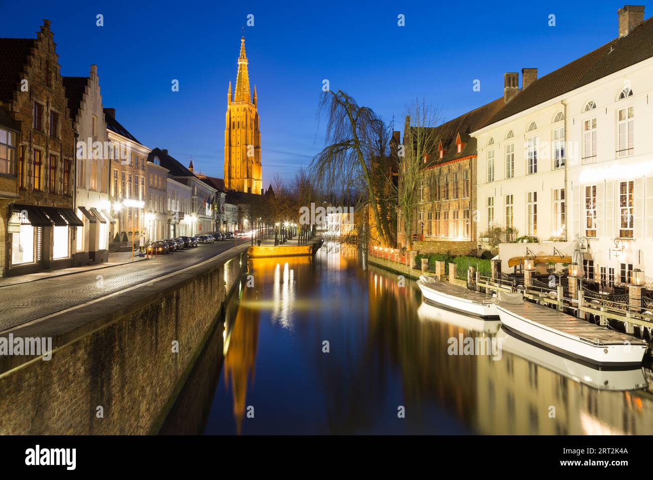 A view along the Dijver canal and street in Bruges during the day in the winter. The Church of Our Lady Bruges can be seen in the distance. There is s Stock Photo