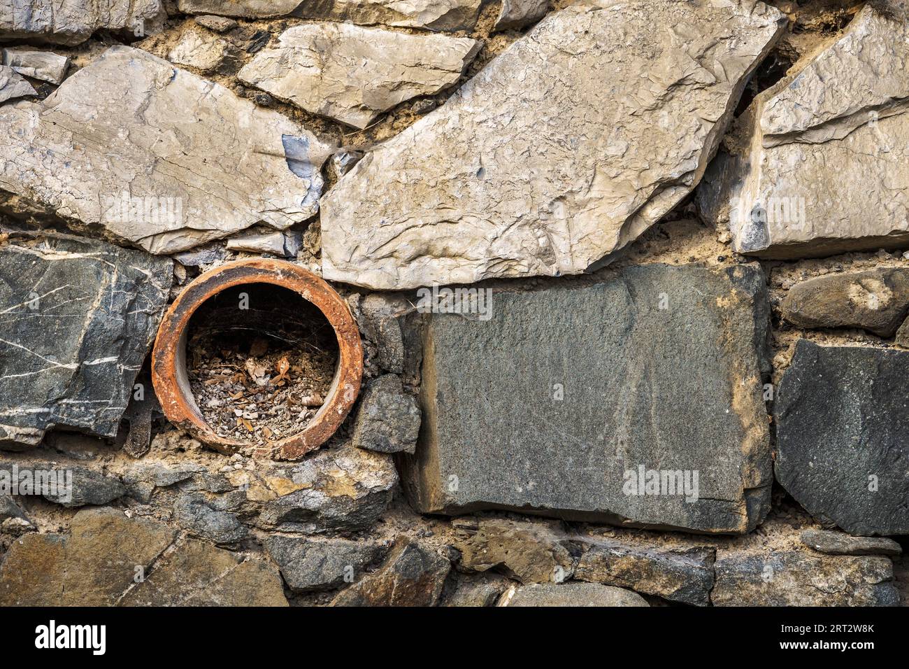 Old drain pipe in the quarry stone wall Stock Photo