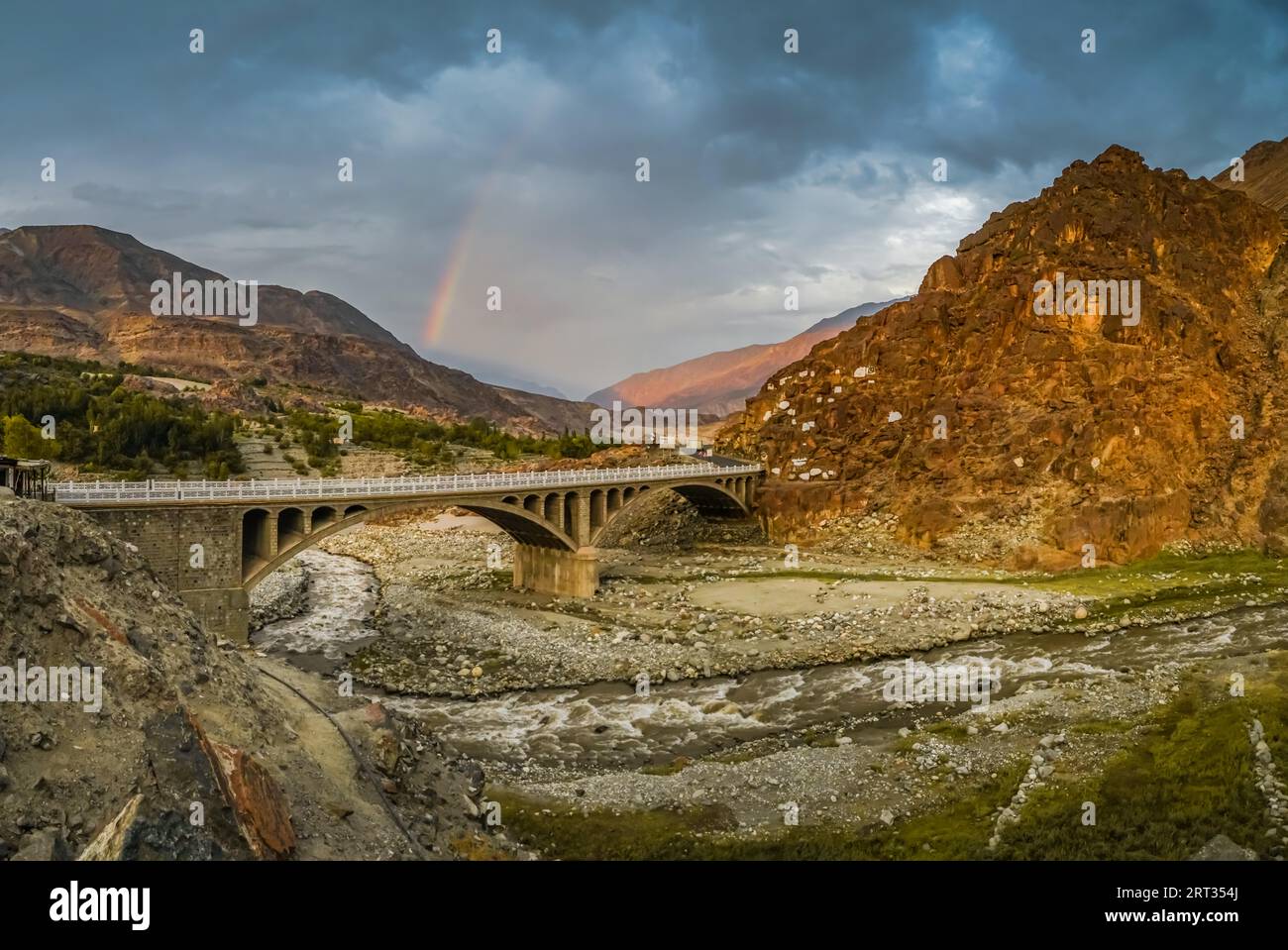 Rainbow in the clouds above bridge crossing river in arid mountains in Pakistan Stock Photo