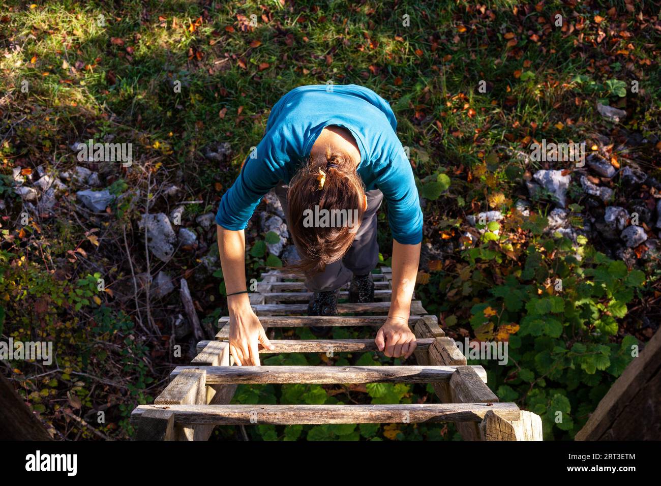 Adult woman wearing blue Sweatshirt climb up a wooden ladder Stock Photo