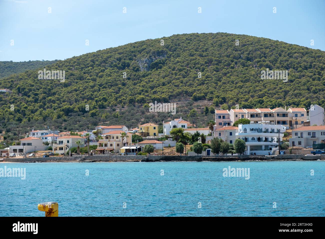 Greece, Megalochori, Milos, Miloi port, Agistri island. Traditional seaside tiled roof building, tree on mountain, calm sea, blue sky, sunny day. Stock Photo