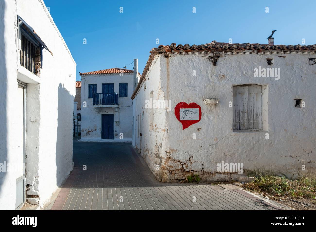Greece, Megalochori, Milos, Miloi village, Agistri island. White paper sign with handwriting direction on red shaped heart at whitewashed building. Stock Photo