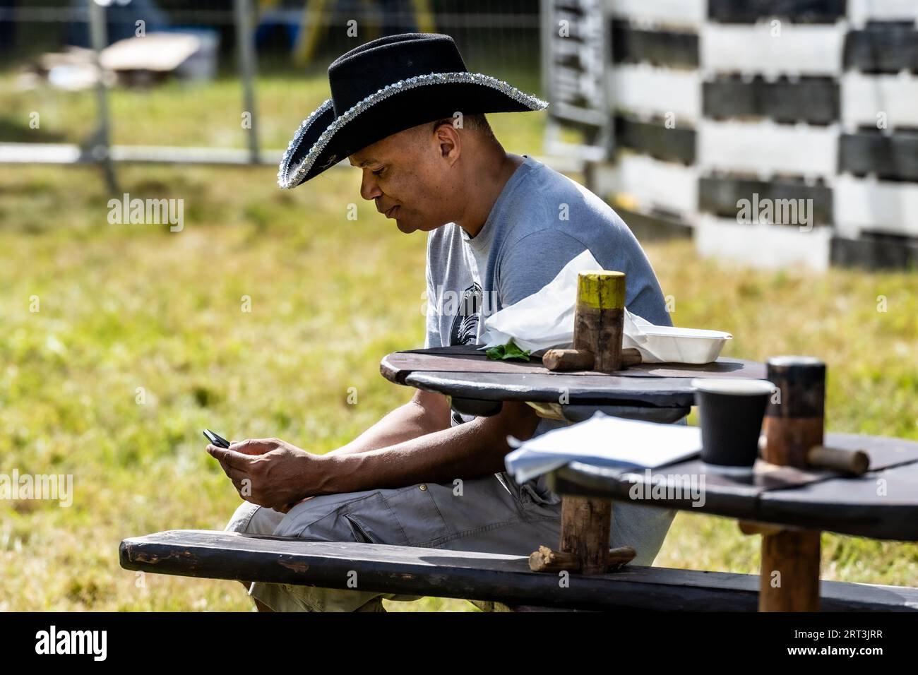 Urban cowboy on his phone. Music festival. Mucky Weekender Festival, Vicarage Farm, Woodmancott, near Winchester, Hampshire, UK Stock Photo