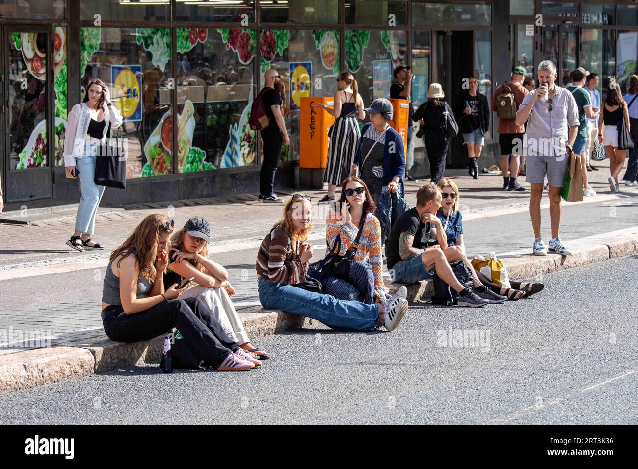 People sitting on the curb in Hämeentie during  Kallio Block Party 2023 in Helsinki, Finland Stock Photo