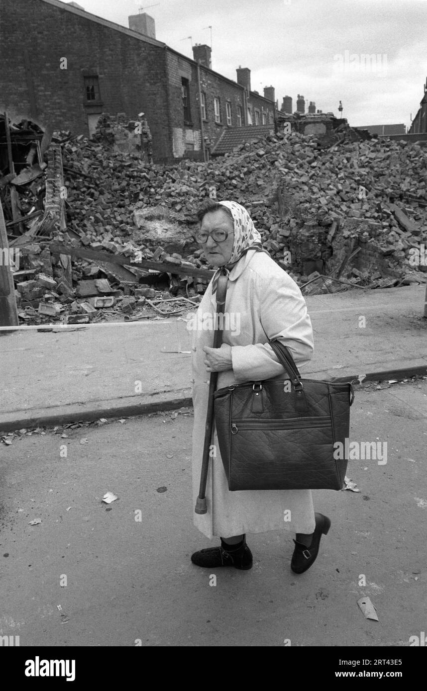 Toxteth Riots 1980s UK. A local old woman out shopping walks past burnt out buildings that have been knocked down to make safe after the riots a day or so before. Toxteth, Liverpool 8, England circa July 1981 HOMER SYKES Stock Photo