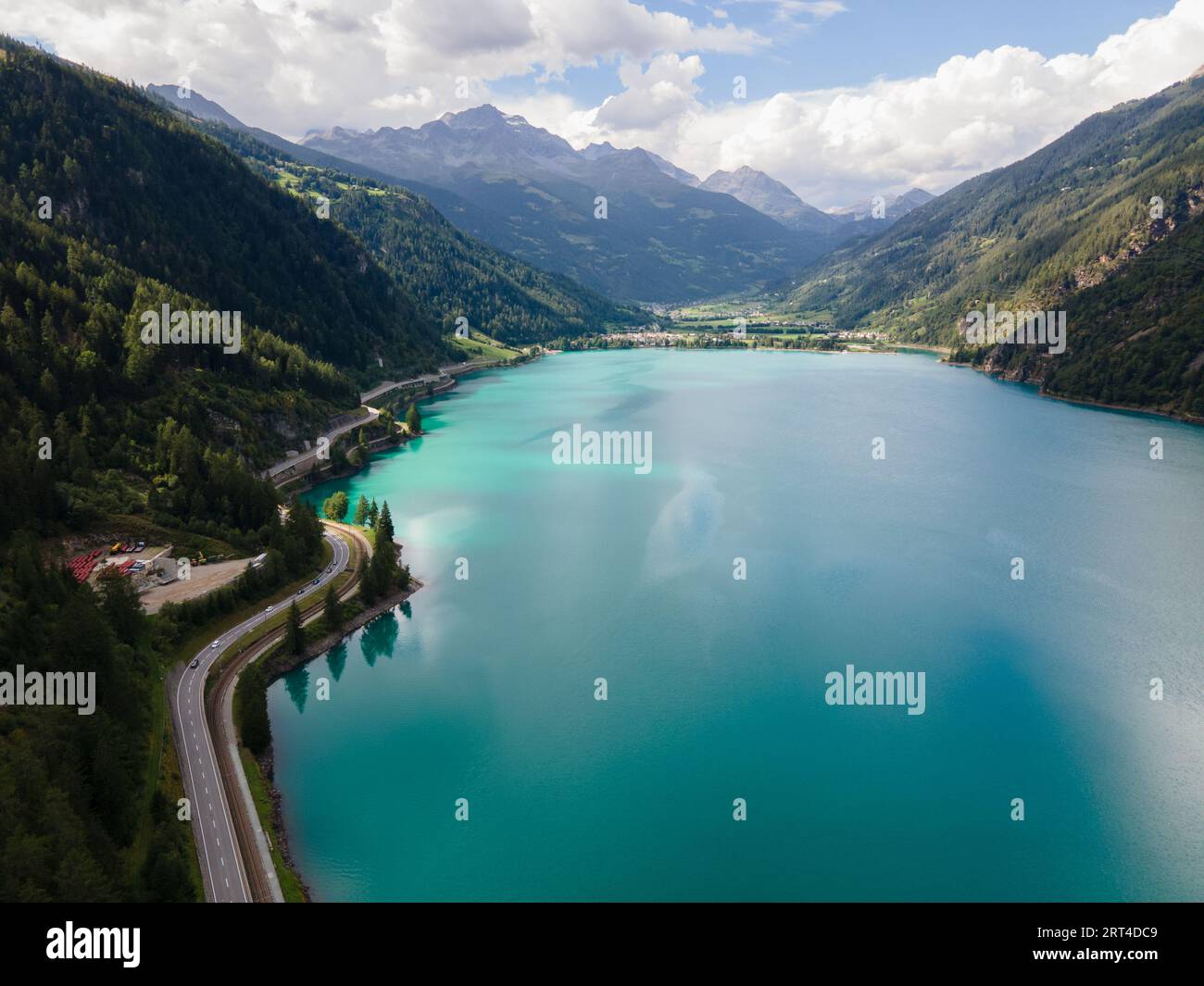 Aerial drone view of Poschiavo alpine lake and road in the Switzerland mountains. Miralago Bernina Express train station. Swiss Alps Stock Photo