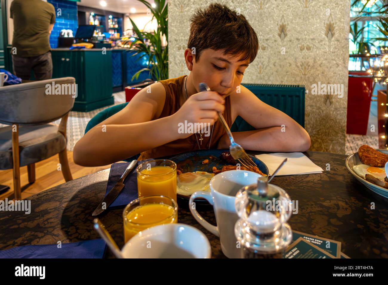 A boy eating a help yourself buffer breakfast at a hotel with a full English items selected including fried egg, beans and a glass of orange juice Stock Photo