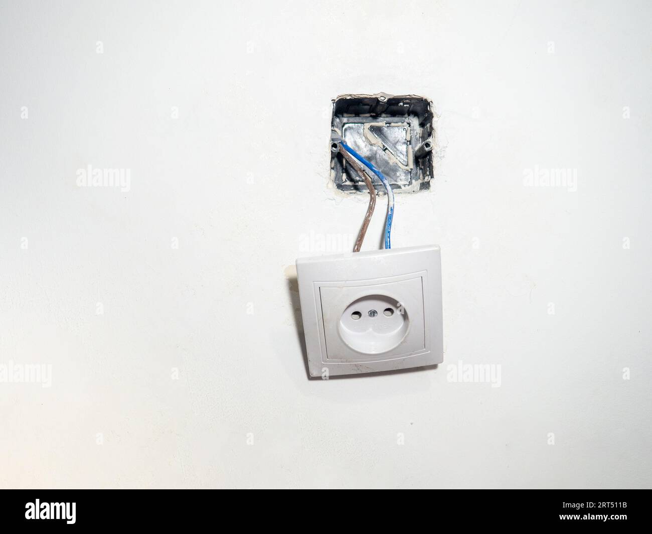 Broken electrical socket on the wall. Disassembled device. White wall