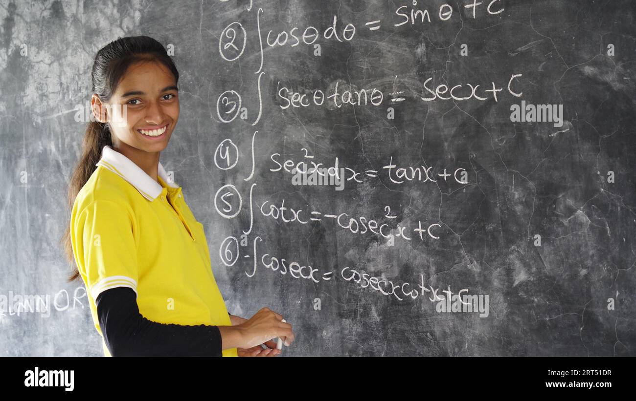 Happy Indian school girl child standing in front of black chalkboard
