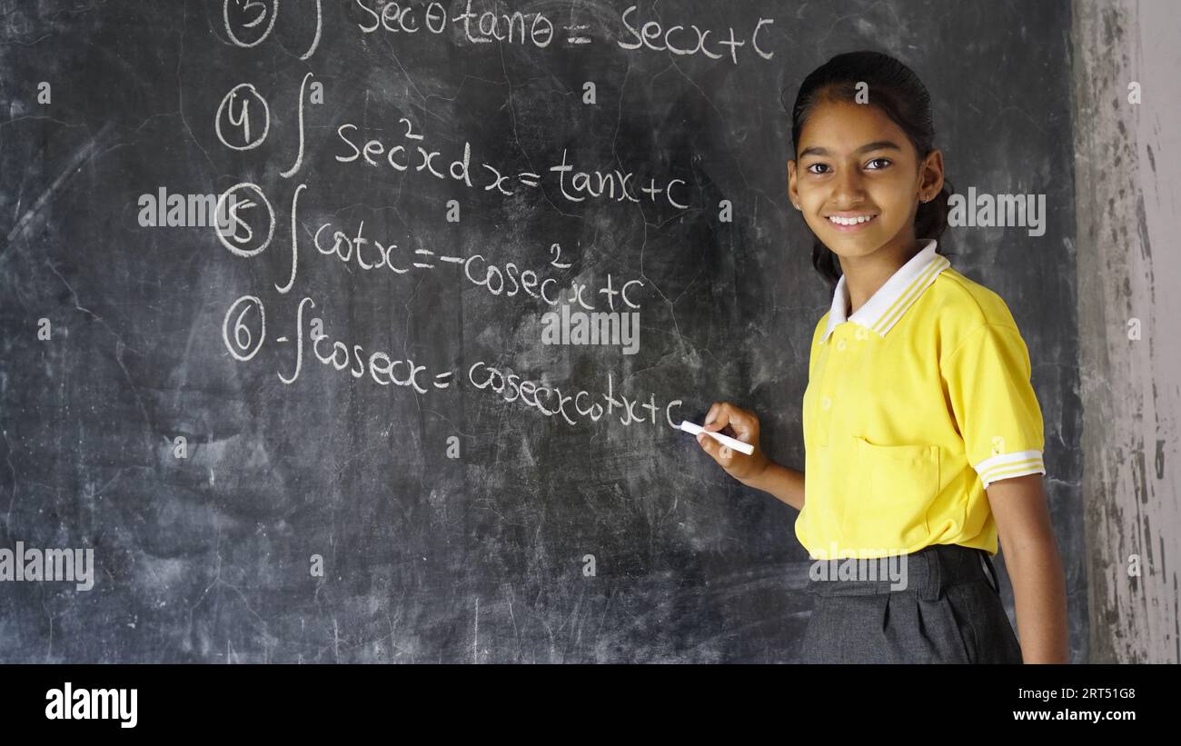 Happy Indian school girl child standing  in front of black chalkboard background. Education Concept or Back to School Stock Photo