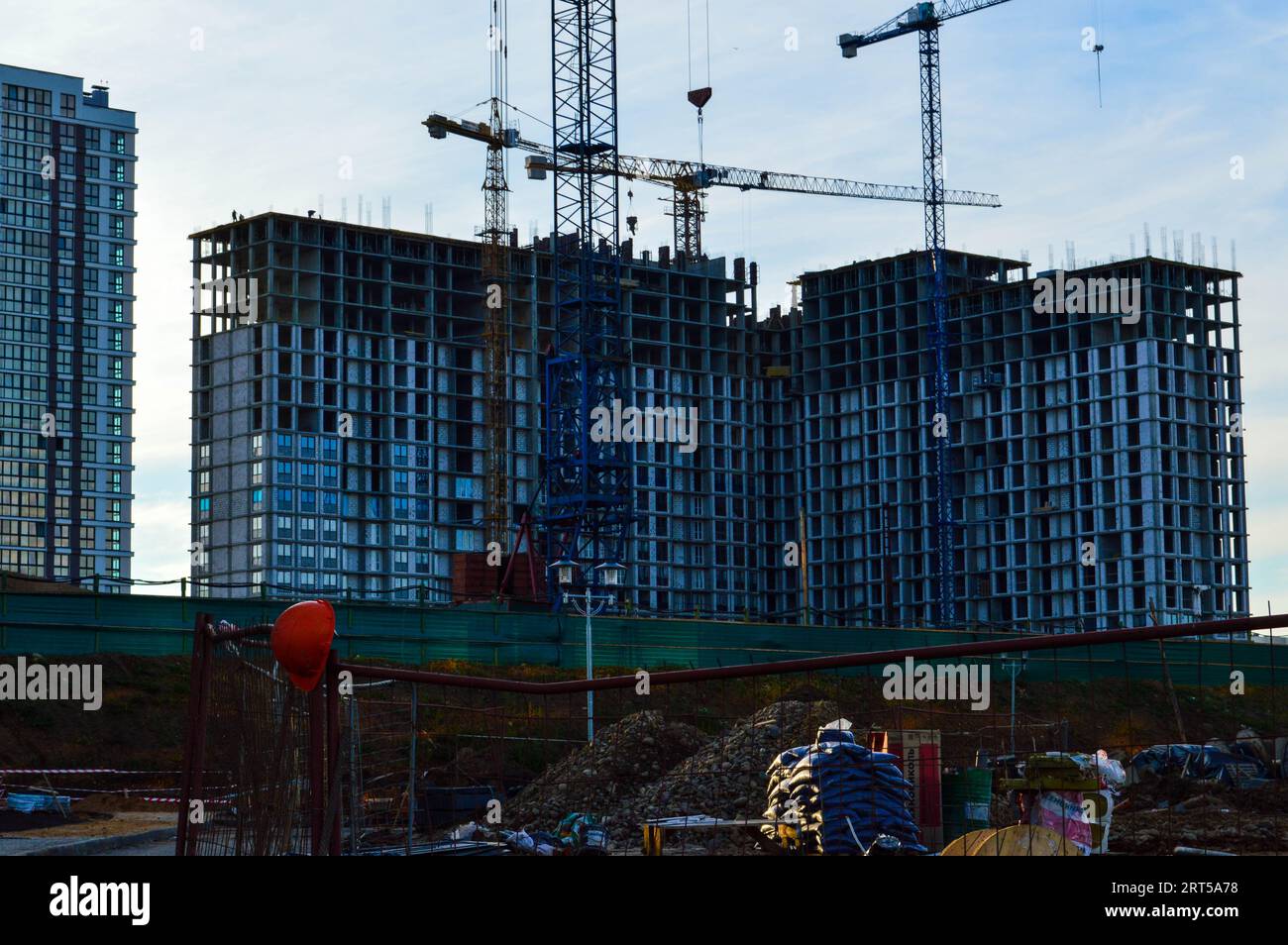 tall concrete houses are being built in the city center. multi-storey buildings, concrete boxes against the backdrop of large cranes for carrying heav Stock Photo
