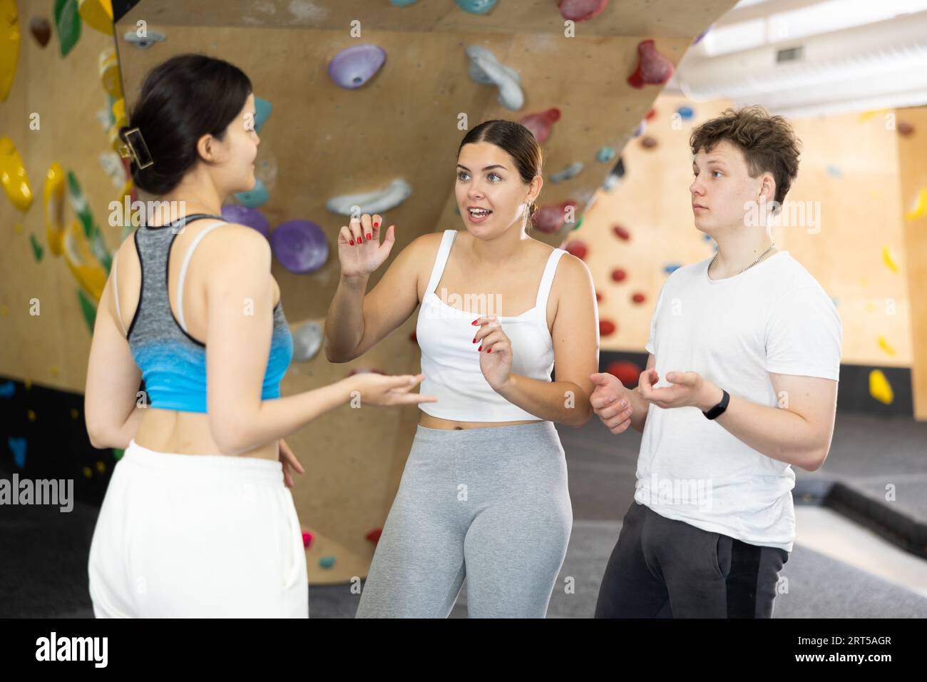 Two young women and teen boy talking at climbing wall Stock Photo