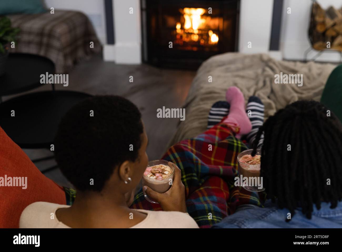 African american couple in socks relaxing at home drinking hot chocolate in front of open fire Stock Photo