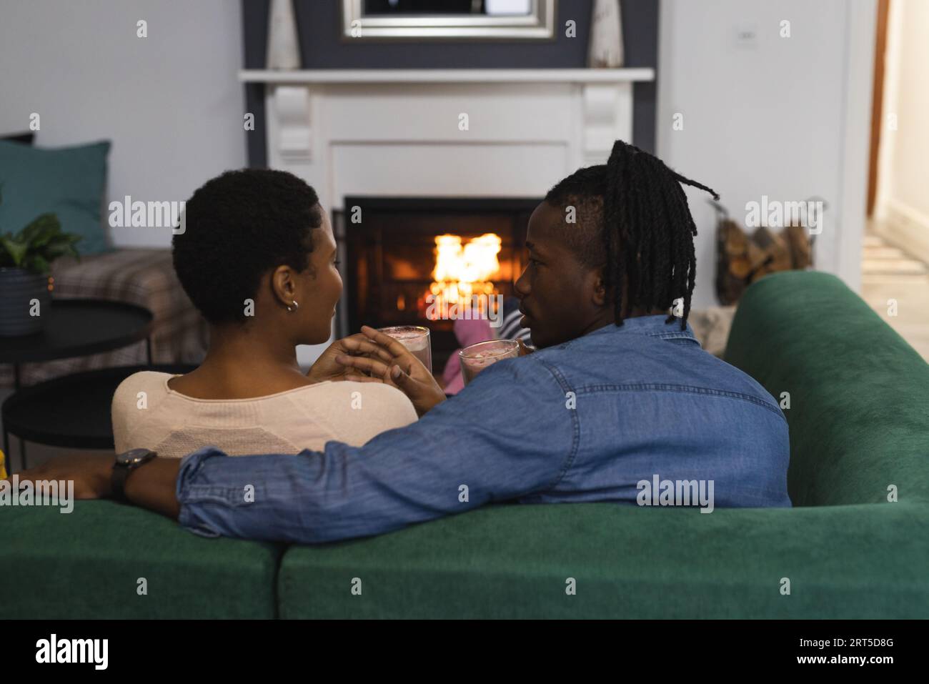 Happy african american couple relaxing at home on couch talking in front of open fire Stock Photo
