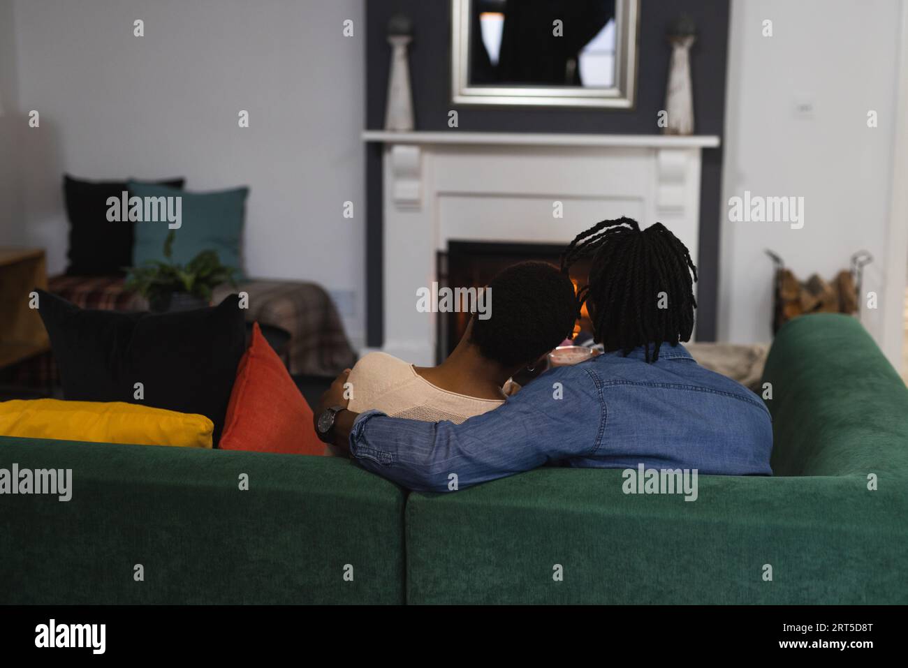 African american couple relaxing at home embracing on couch in front of open fire Stock Photo