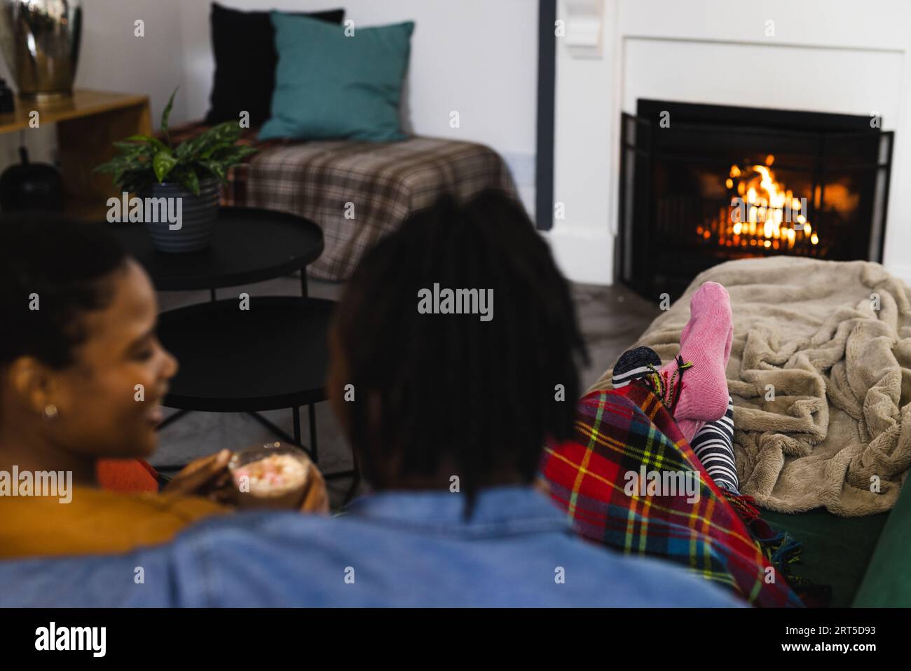 Happy african american couple in socks relaxing at home in front of open fire with hot chocolate Stock Photo