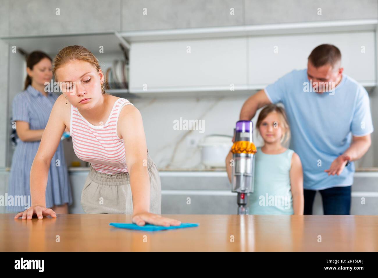 Teenage daughter dusting the table while parents and youngest daughter ...