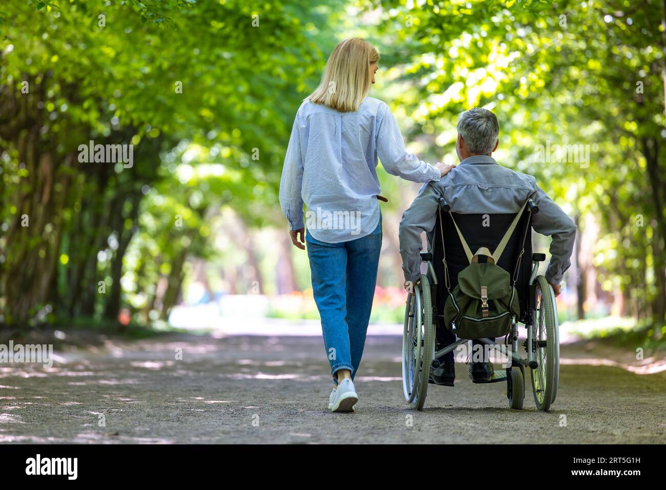 Man in wheelchair walking at park with his wife Stock Photo - Alamy