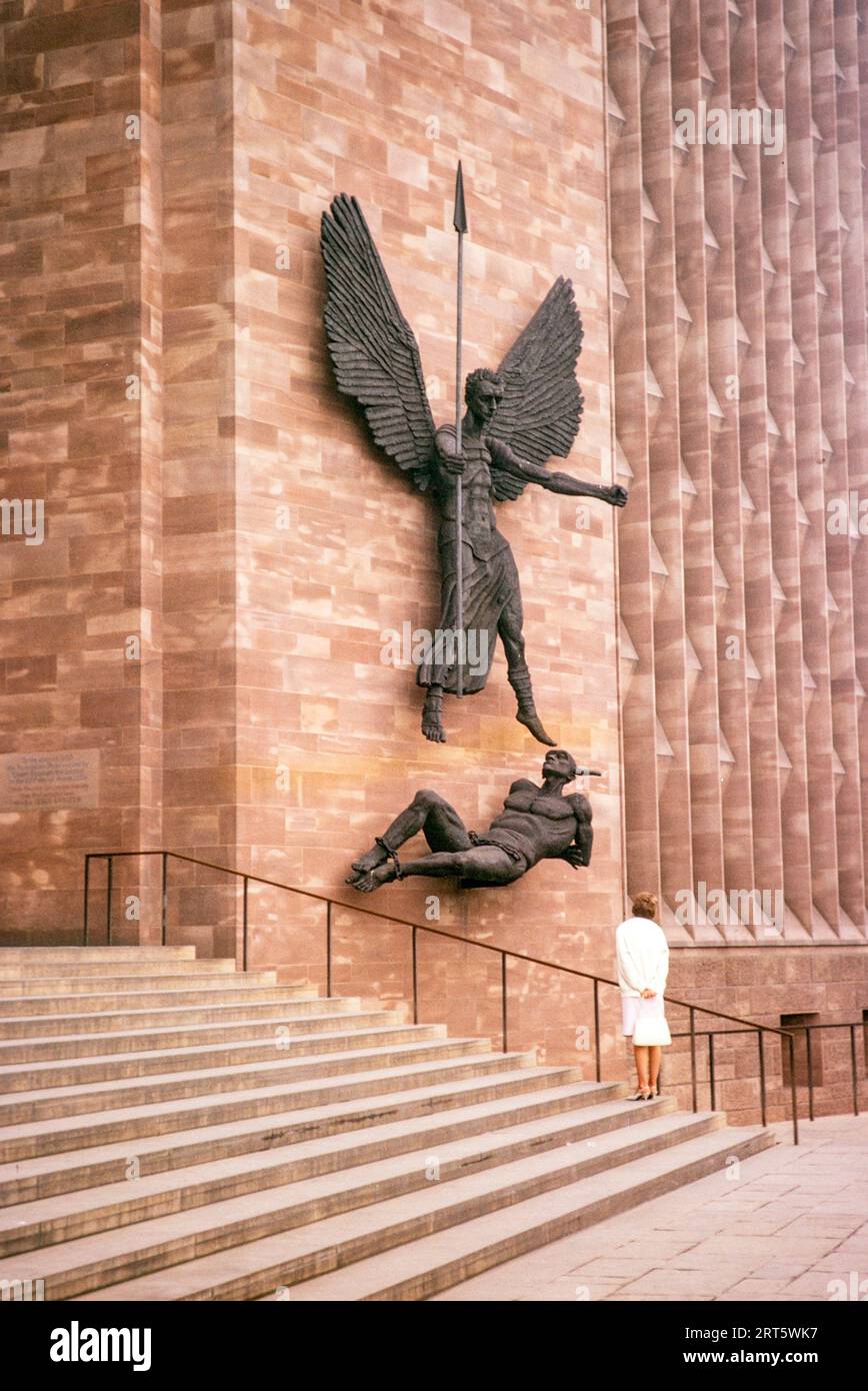 Woman standing looking at sculpture Coventry cathedral church, West Midlands, England, UK, March 1966 'St Michael's Victory over the Devil' 1958 bronze sculpture by Jacob Epstein, Stock Photo