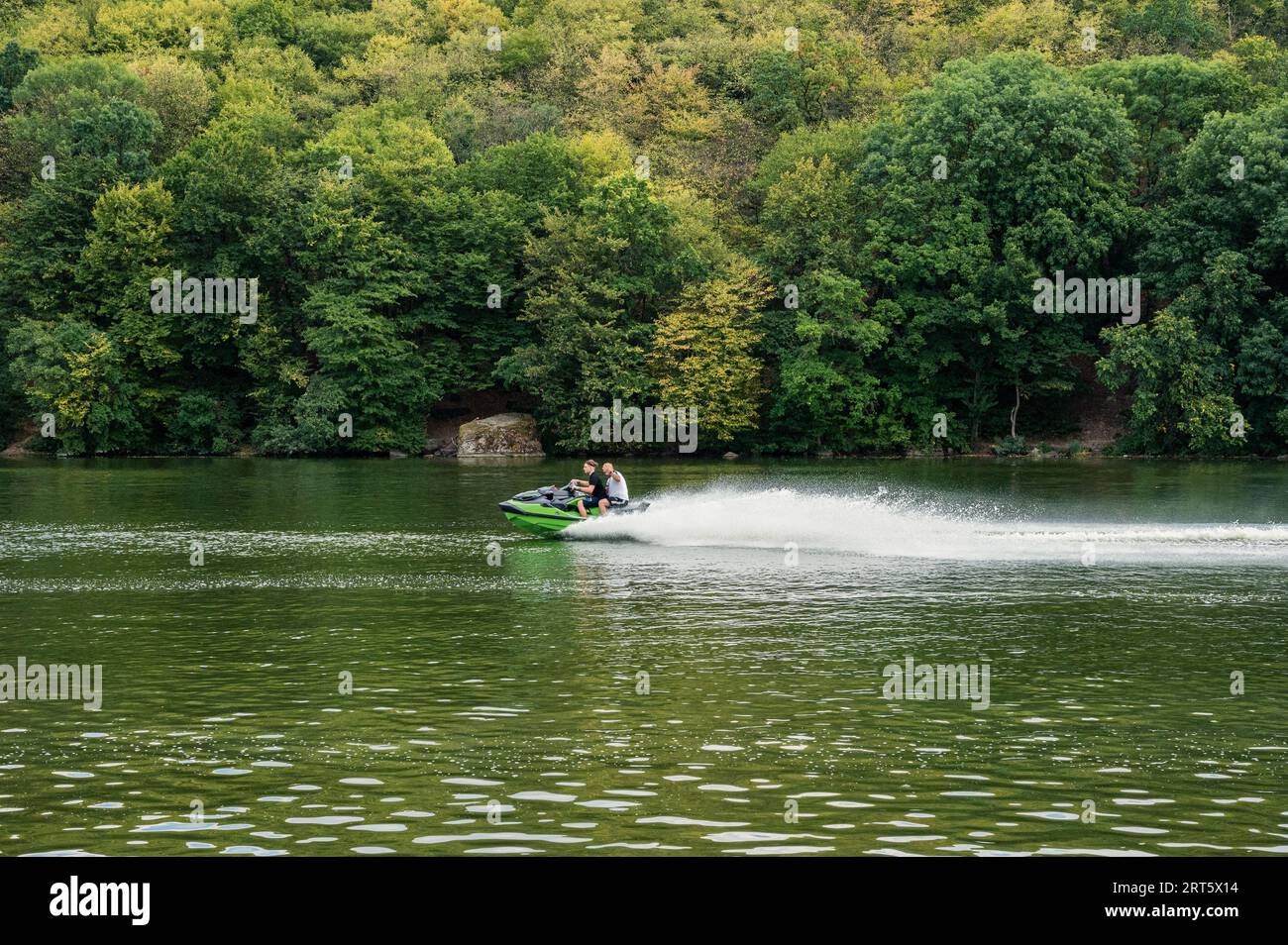 Two people riding jet ski watercraft on river with beautiful green trees background. Speed, sport, vacation, extreme Stock Photo