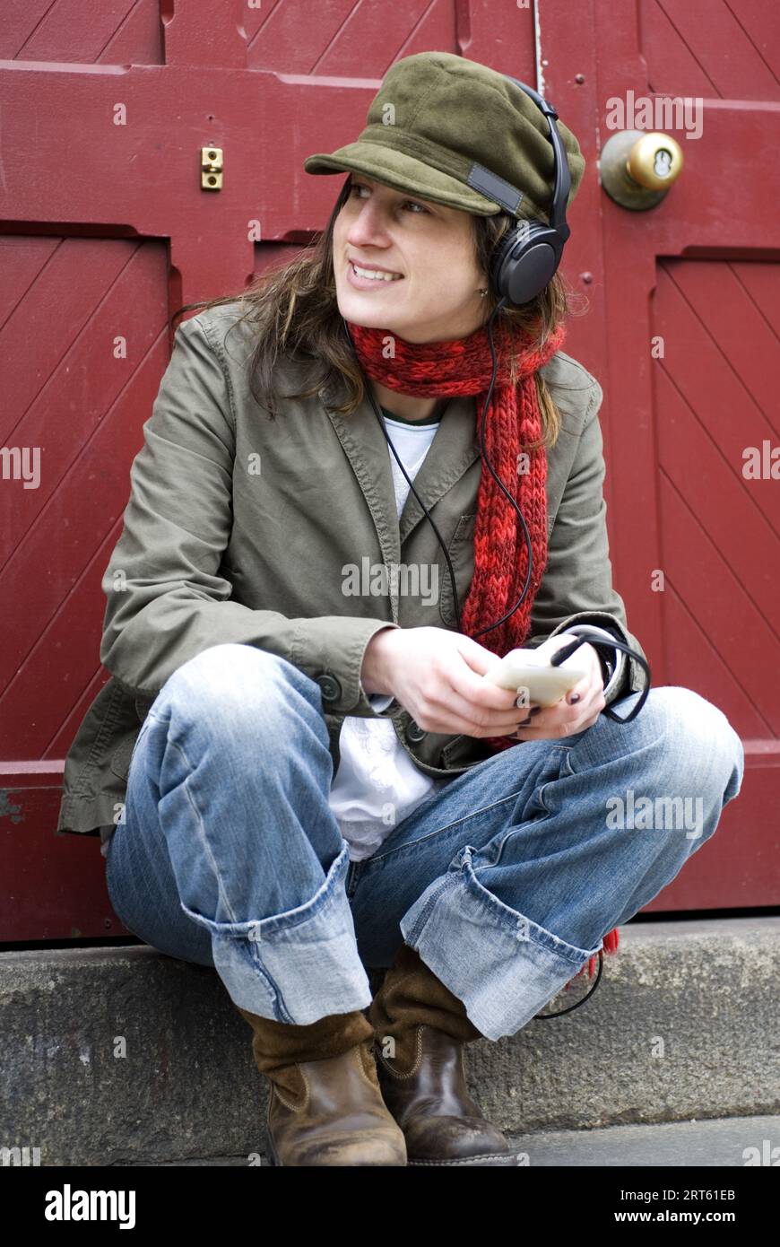 Hip woman relaxes infront of red door while listening to music on Ipod. Boston, MA. Stock Photo