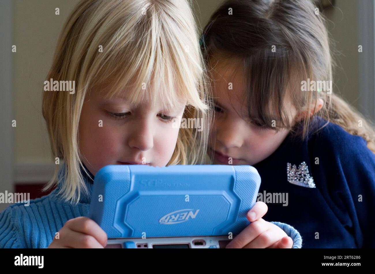 Two girls (5-6 years) playing a hand held video game. Stock Photo