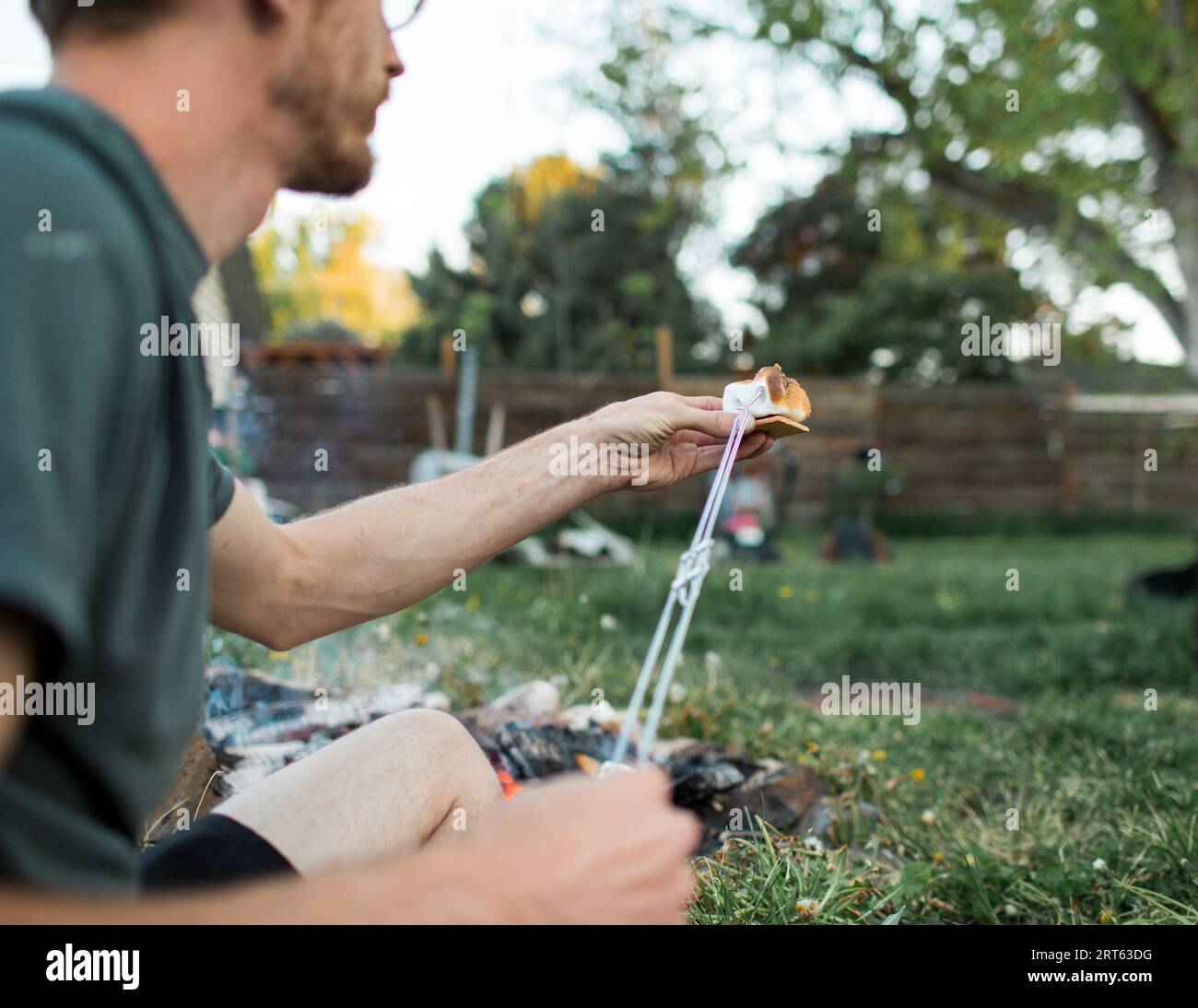 Man assembles s’more with campfire behind Stock Photo