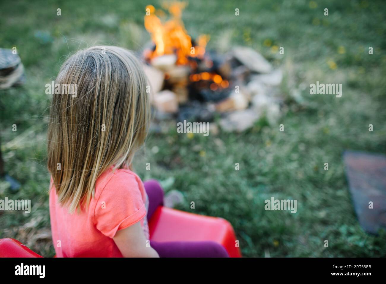 Toddler in red chair awaits s’mores by campfire. Stock Photo