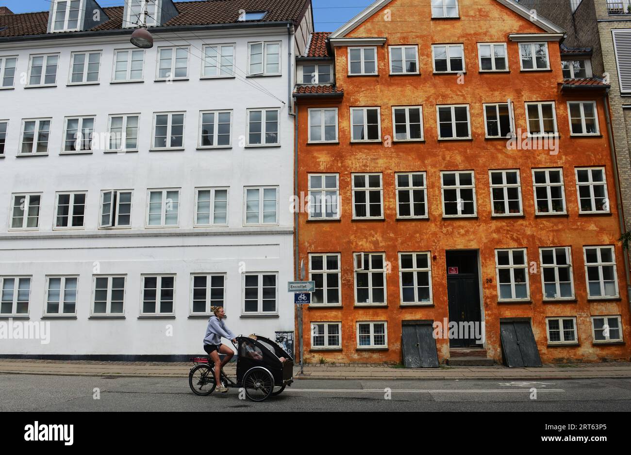 A Danish woman cycling in front of a Colorful building along Åbenrå in central Copenhagen, Denmark. Stock Photo