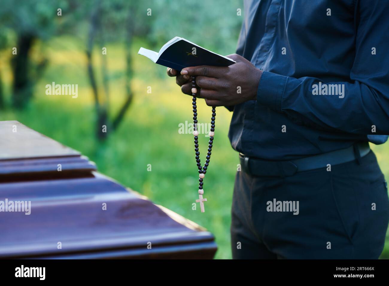 Close-up of African American man in priest attire holding rosary beads ...