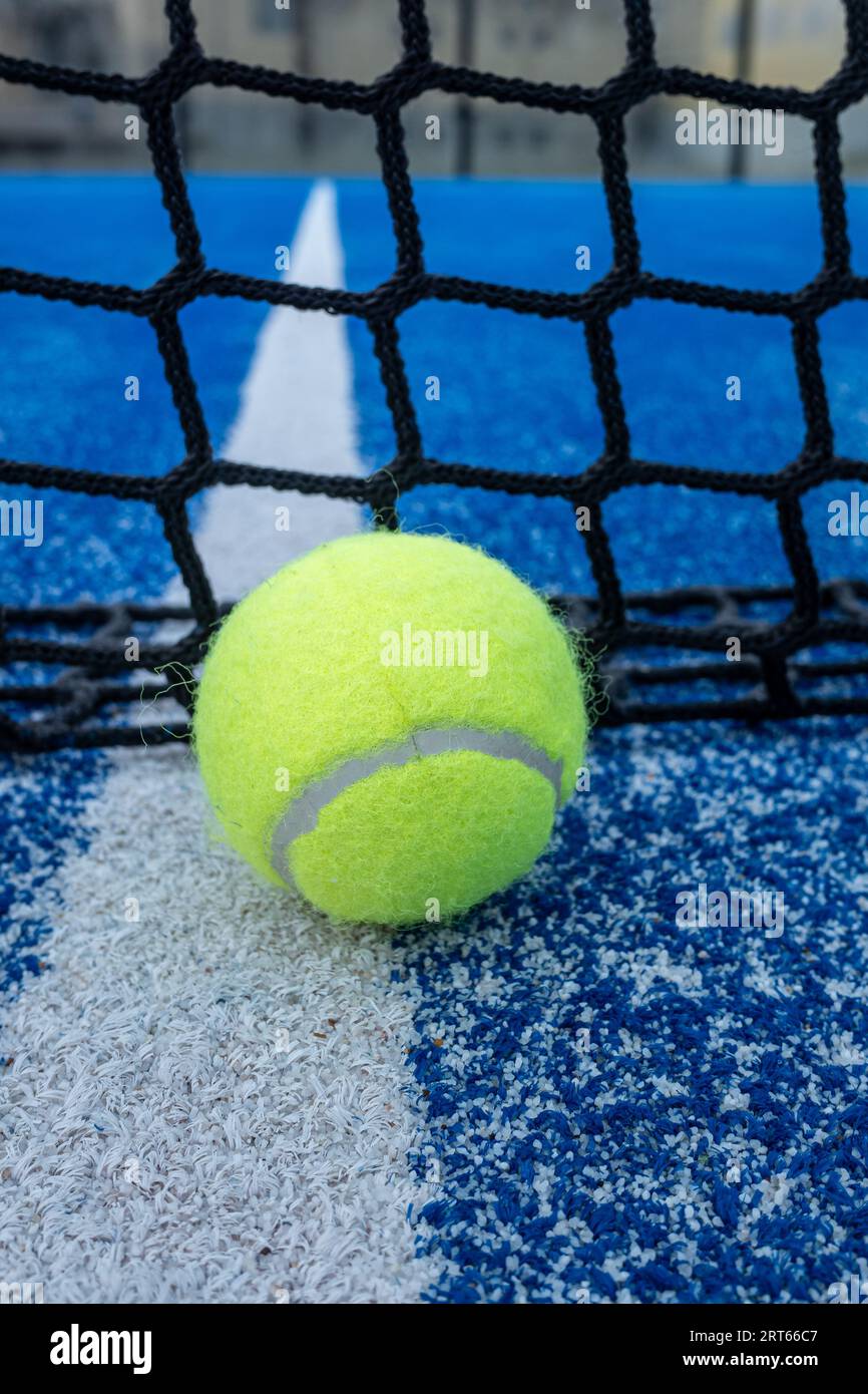 Yellow ball on floor in front of paddle net in blue court outdoors. Padel tennis Stock Photo