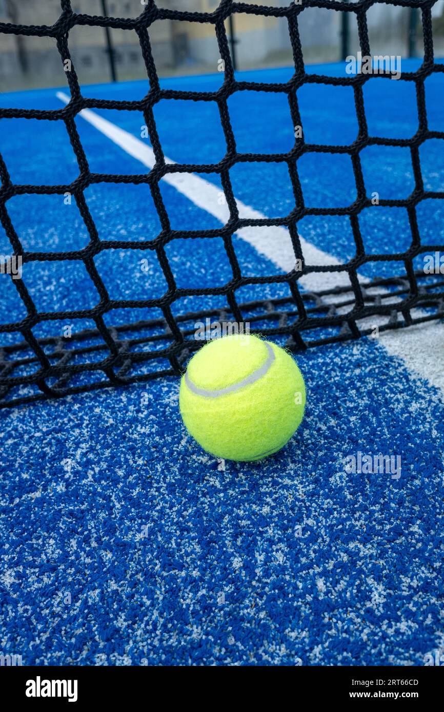 Yellow ball on floor in front of paddle net in blue court outdoors. Padel tennis court Stock Photo