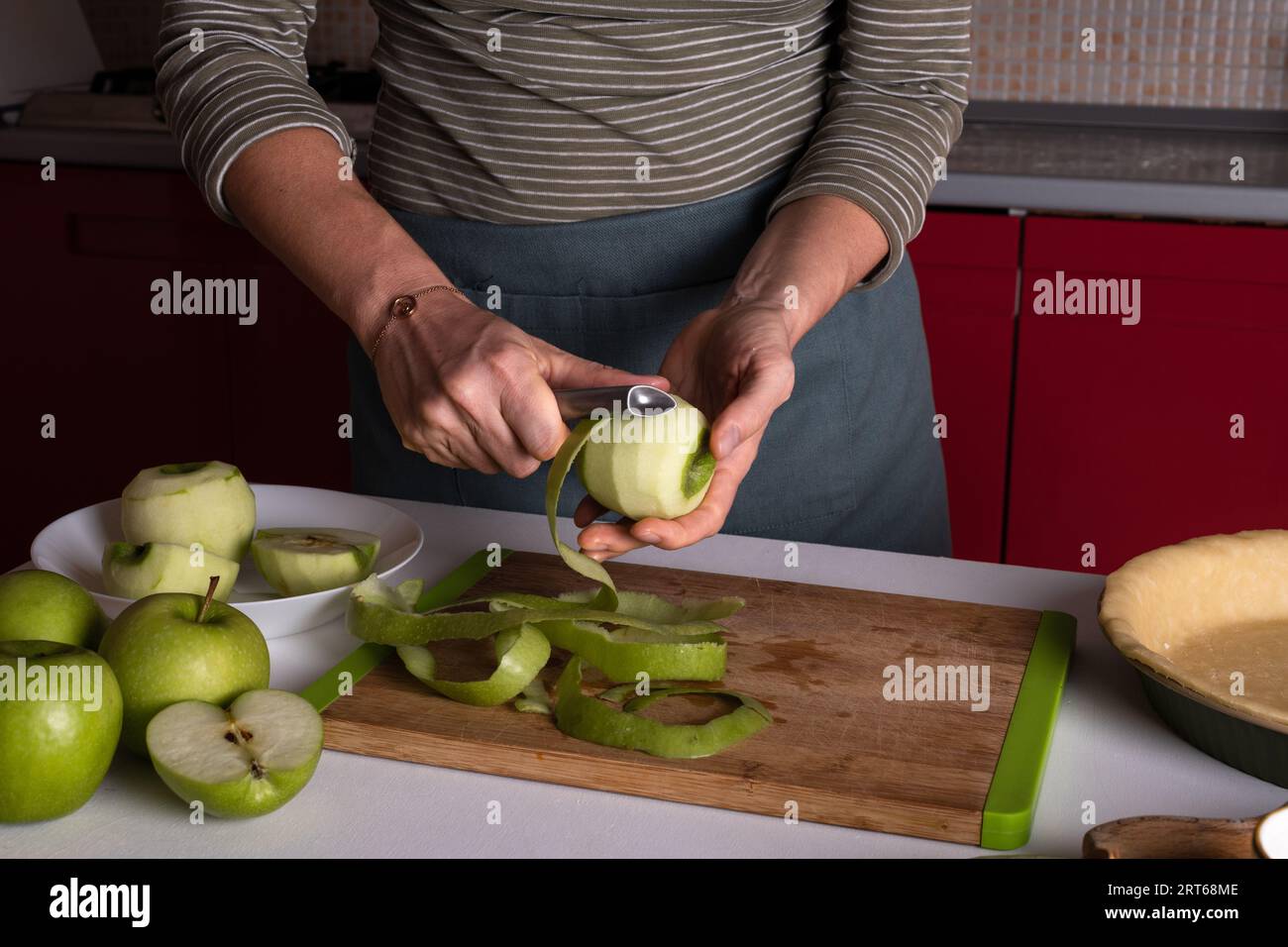 Woman is peeling apples to prepare apple pie in the kitchen. Authentic