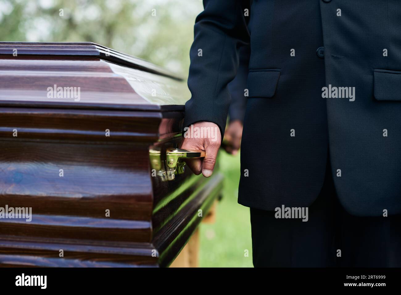 Closeup of man in black suit holding by handle of wooden coffin with